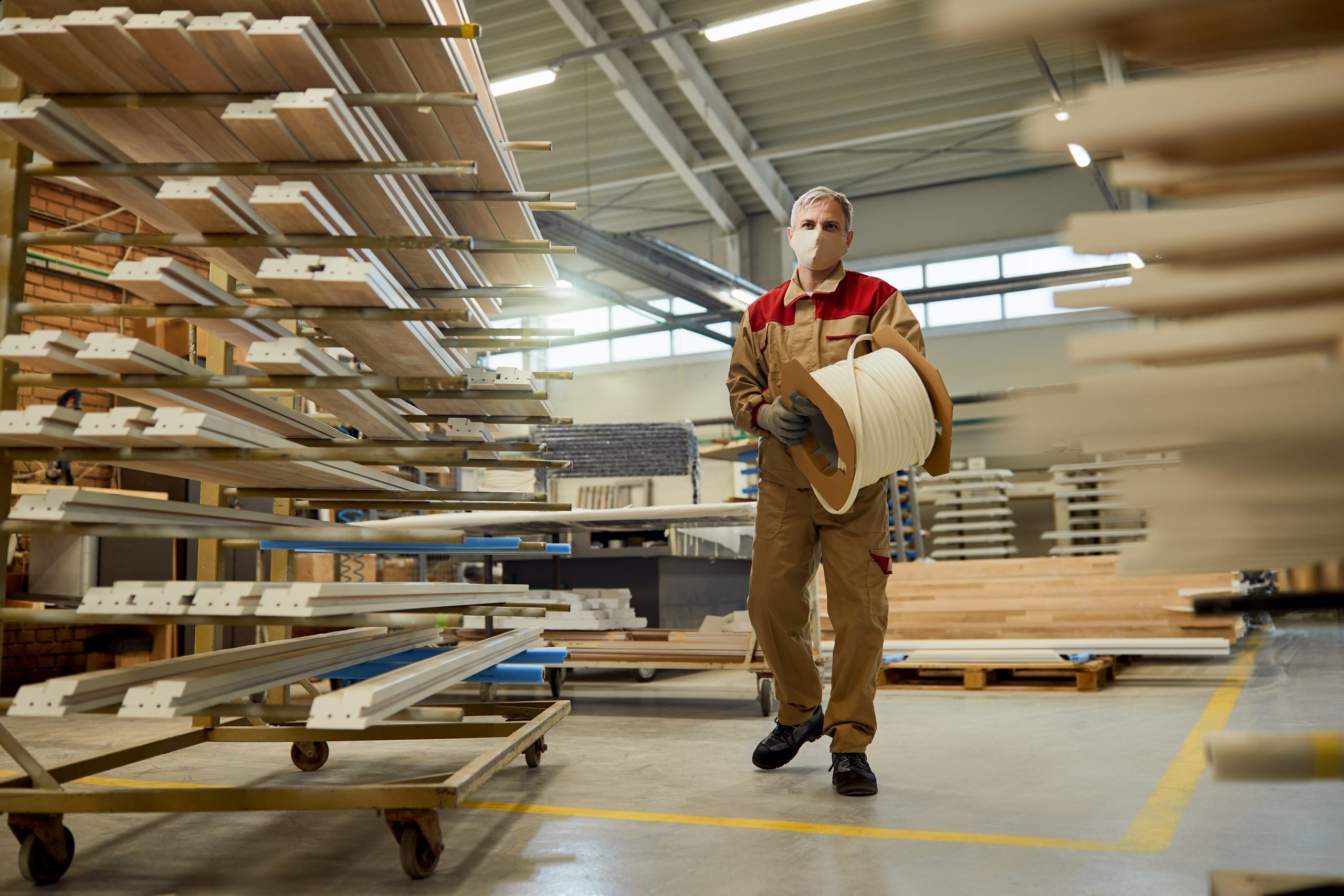 Full length of carpenter carrying protective foam while working in a workshop during COVID-19 pandemic.